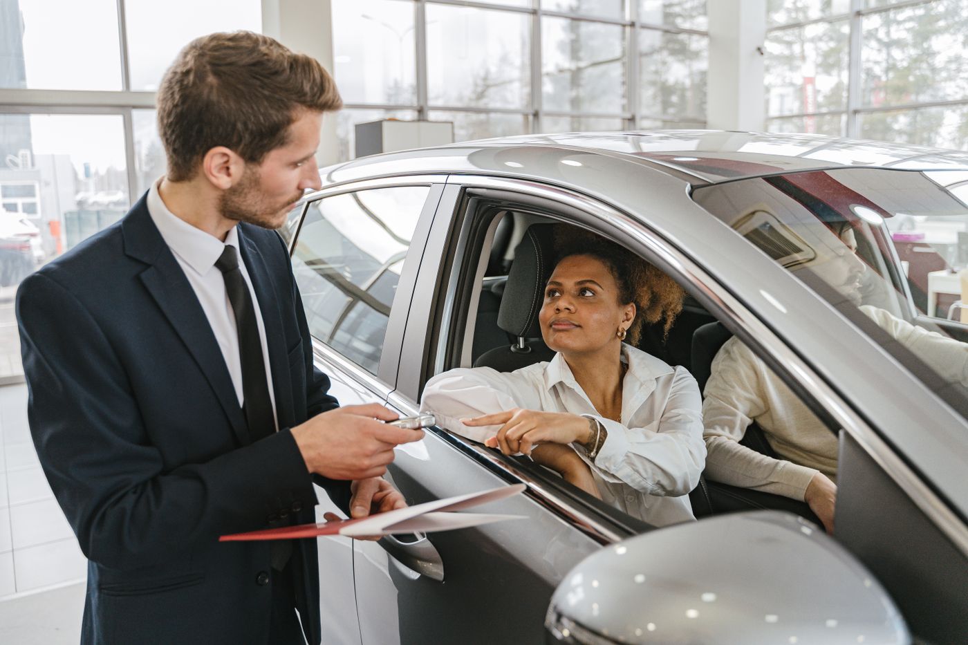 Vendedor entregando a chave para uma cliente sentada em um carro novo, dentro da loja
